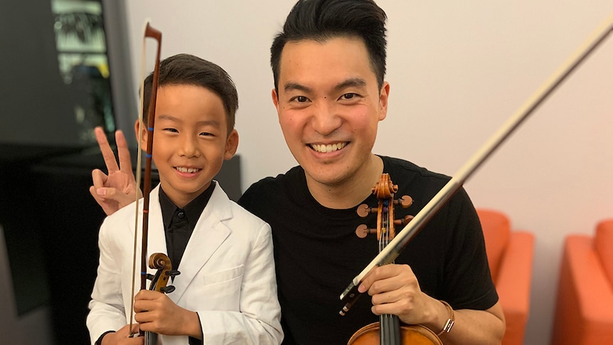 7-year-old Allen Wang poses with Australian violinist Ray Chen. Both are holding violins and Ray holds up bunny-ears fingers.