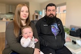 A man and a woman sitting inside their home with their baby.