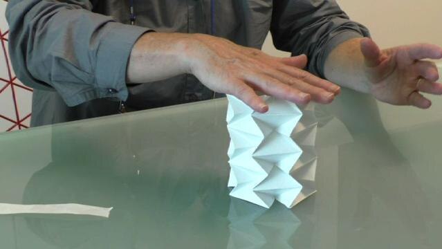Hands sit on top of paper folded into a complex cylinder shape