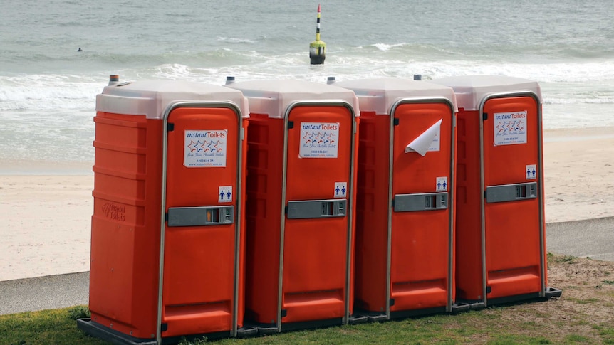 Four orange portable toilets line Cottesloe Beach.