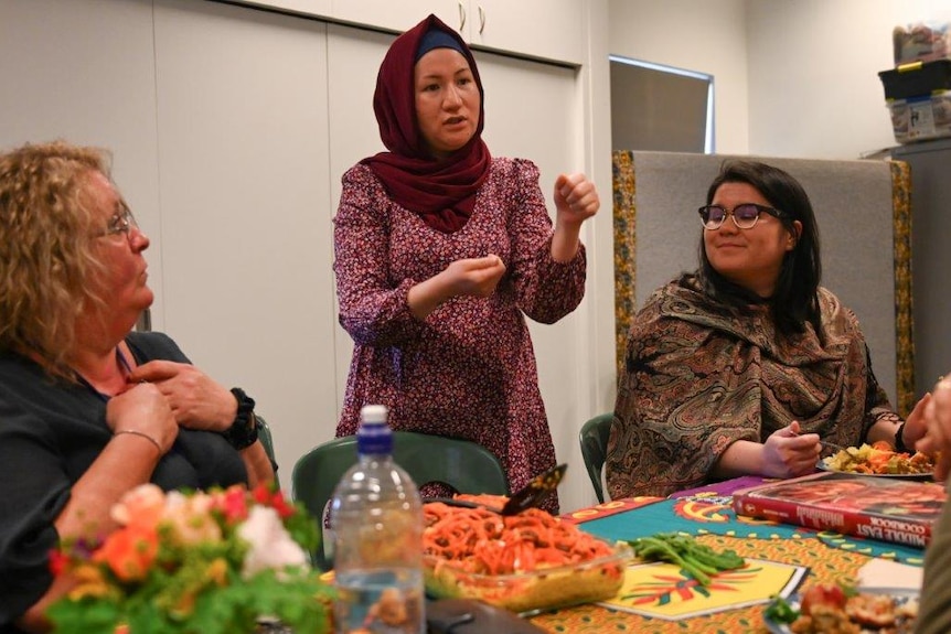 A woman stands in front of a table giving a presentation