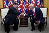 Two men shaking hands while seated before a row of North Korean and US flags