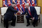 Two men shaking hands while seated before a row of North Korean and US flags