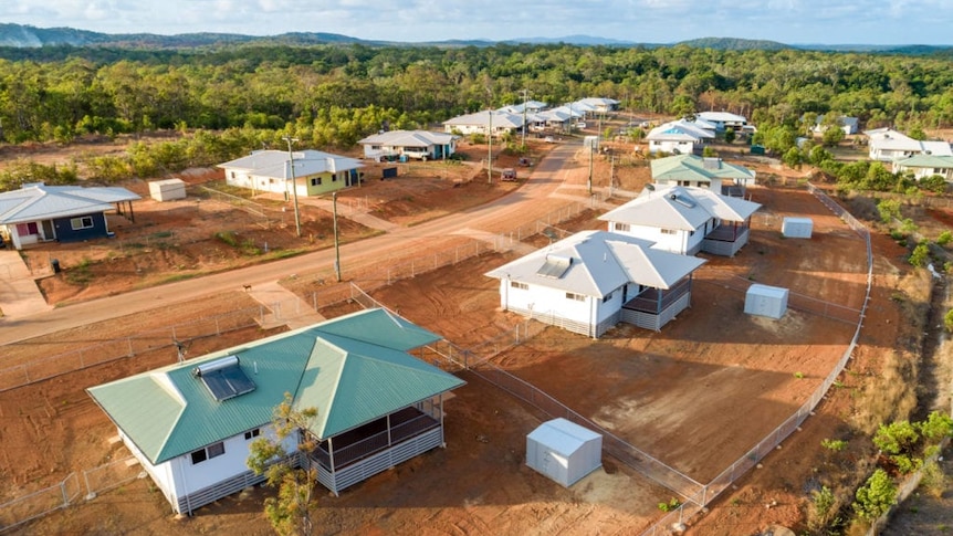 An aerial view of a new housing estate on red dirt surrounded by trees.