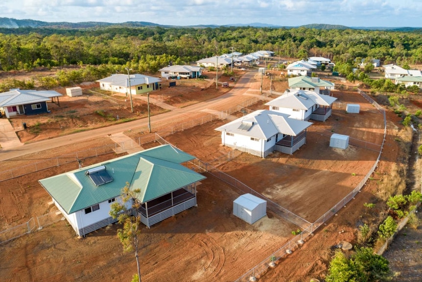 An aerial view of a new housing estate on red dirt surrounded by trees.