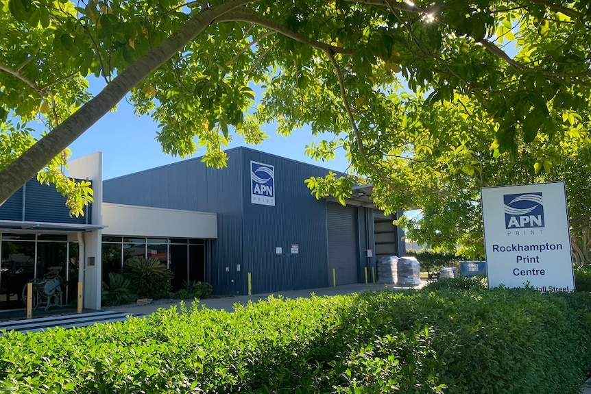 The outside of the APN Print Rockhampton building behind a green hedge and tree.