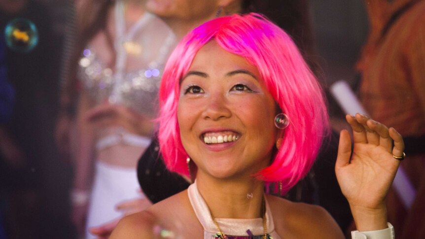 A girl wearing a pink wig smiling and looking like she's having fun.