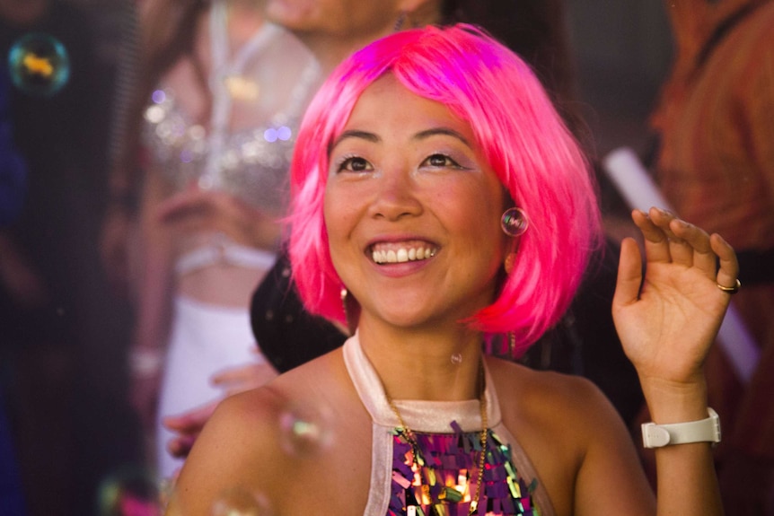 A girl wearing a pink wig smiling and looking like she's having fun.