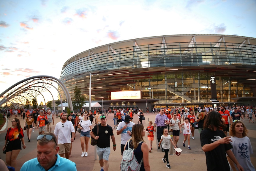 Dozens of cricket fans stream out of Perth Stadium towards the train station as the sun goes down.