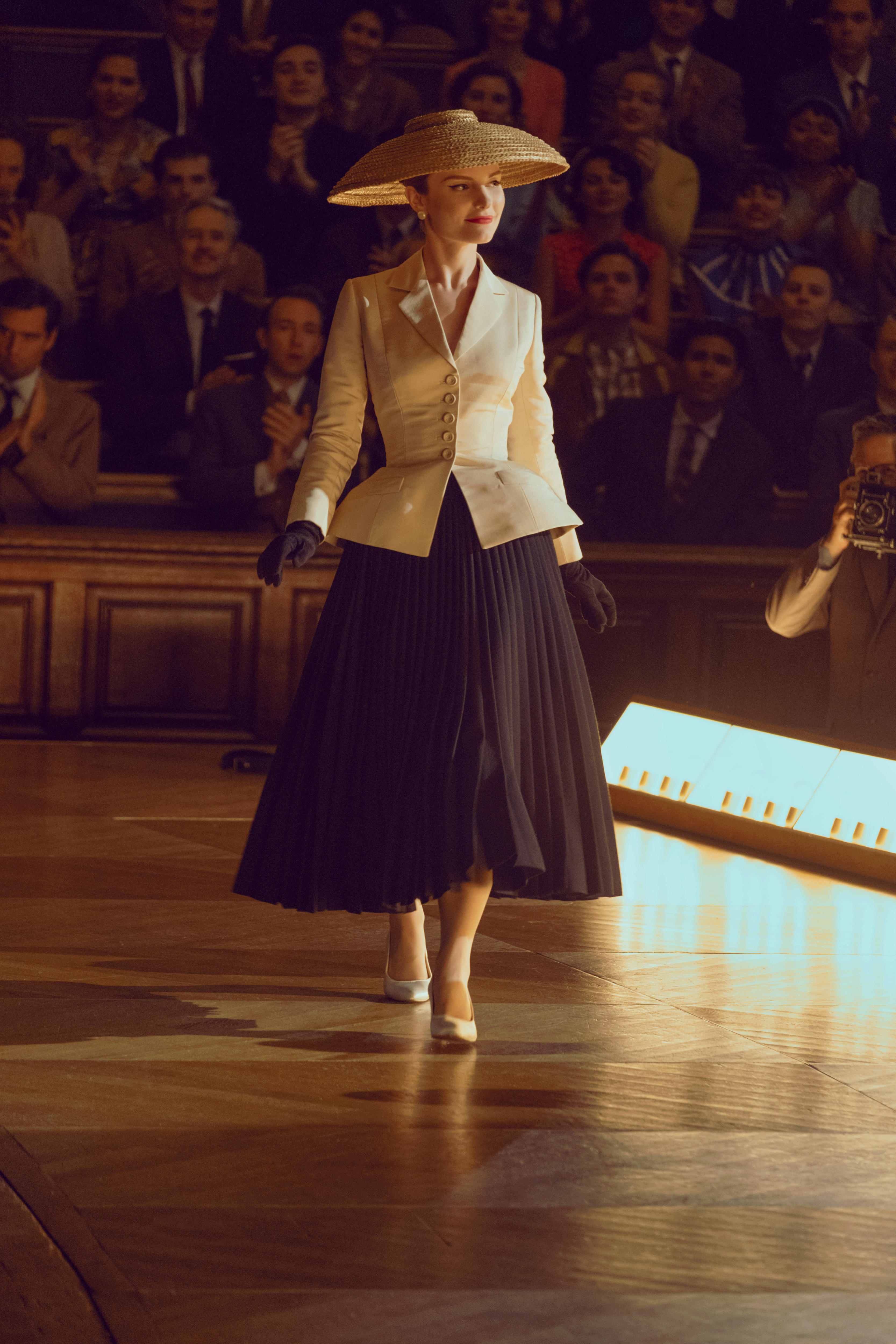 A model wearing Dior's designs - a big black pleated skirt, a heavily sinched white jacket and a broad white hat.