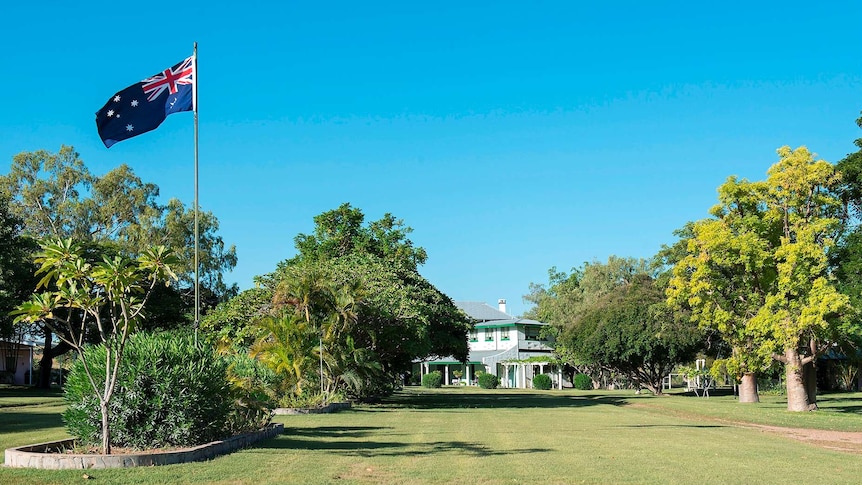 Fossil Downs homestead and surrounding lawn and garden with clear blue sky and Australian flag flying high