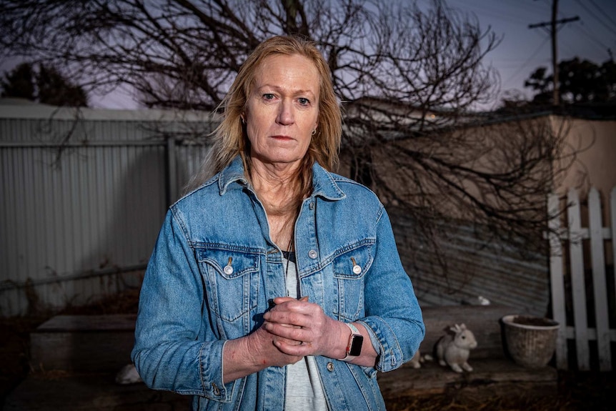 Donna stands in her backyard with her hands clasped together, with a powerline in the background.