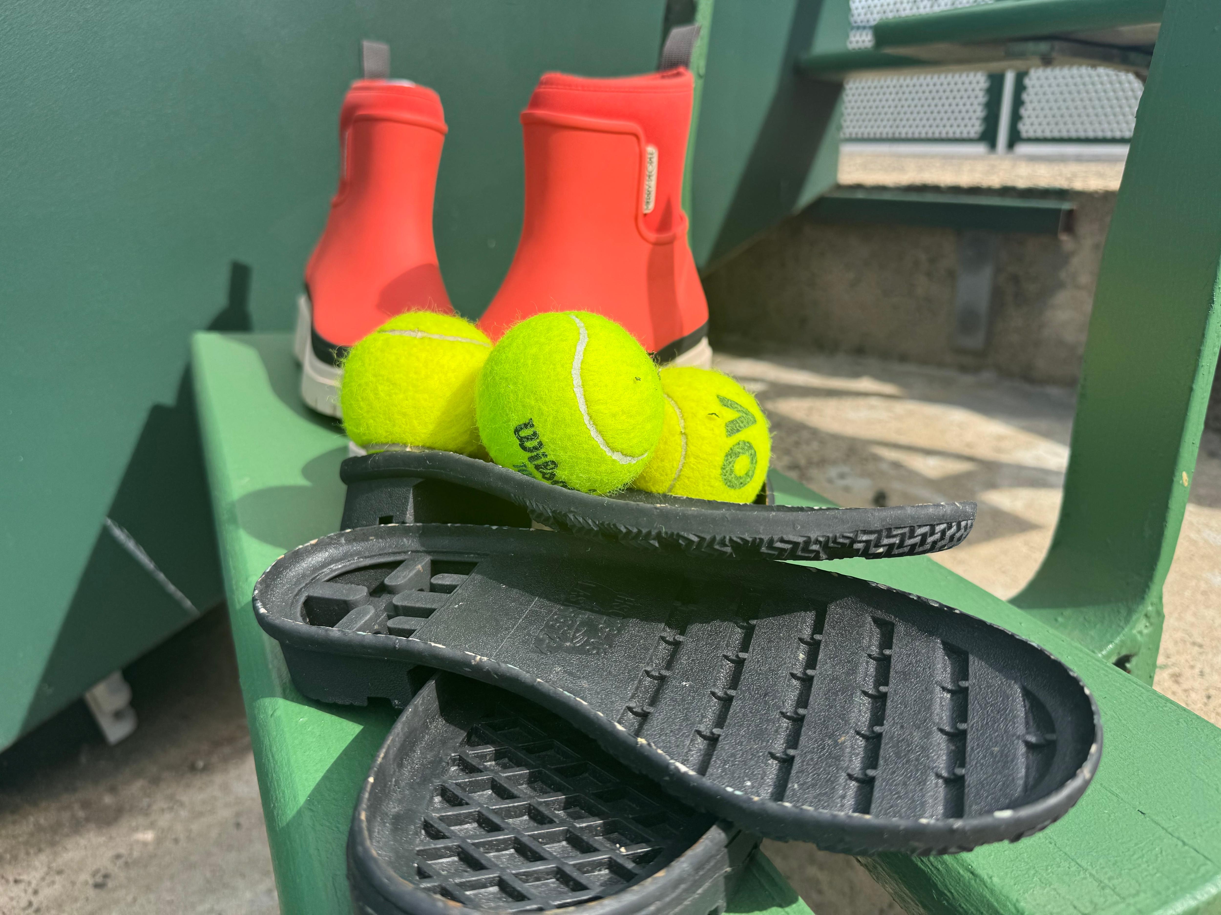 Pelotas de tenis, zapatos y suelas de zapatos se encuentran sobre una silla.