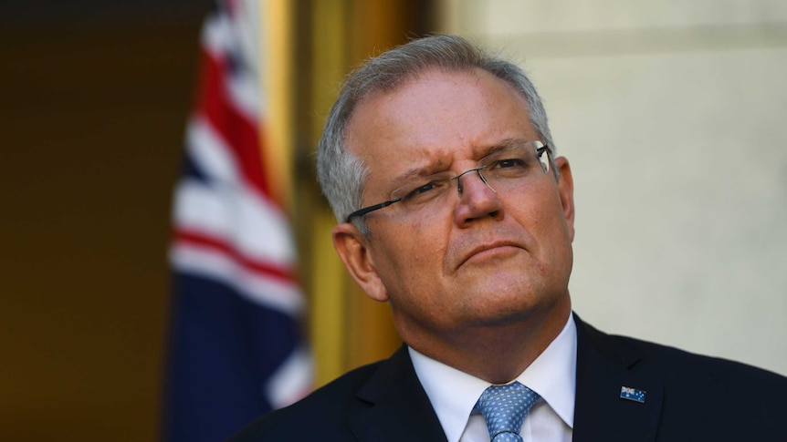 Morrison looks pensive in front of a flag