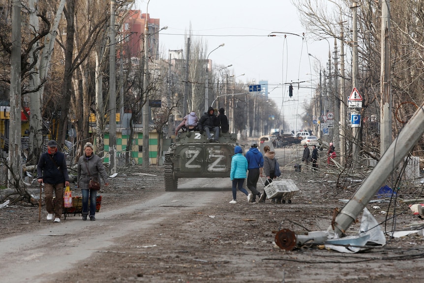 A Russian armoured vehicle with 'Z' painted on it moves down a street covered in debris