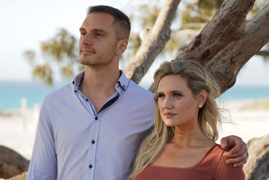 A mid-shot of a young woman and a young man standing side by side posing for a photo outdoors and looking off camera.