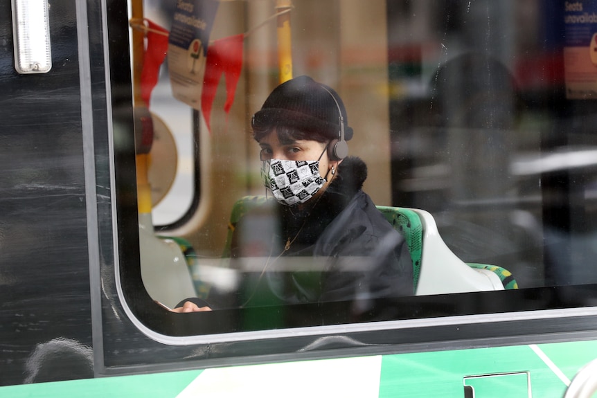 A person sits on a tram wearing a mask.