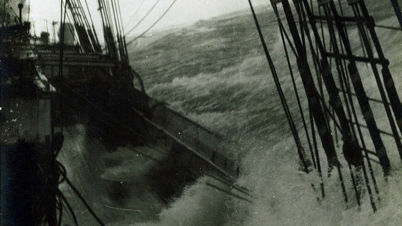 A tall ship sails through rough seas.