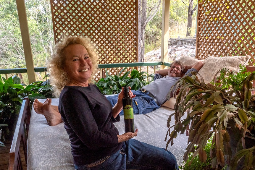 A man lays on a bed while a woman holds a bottle of sauce.