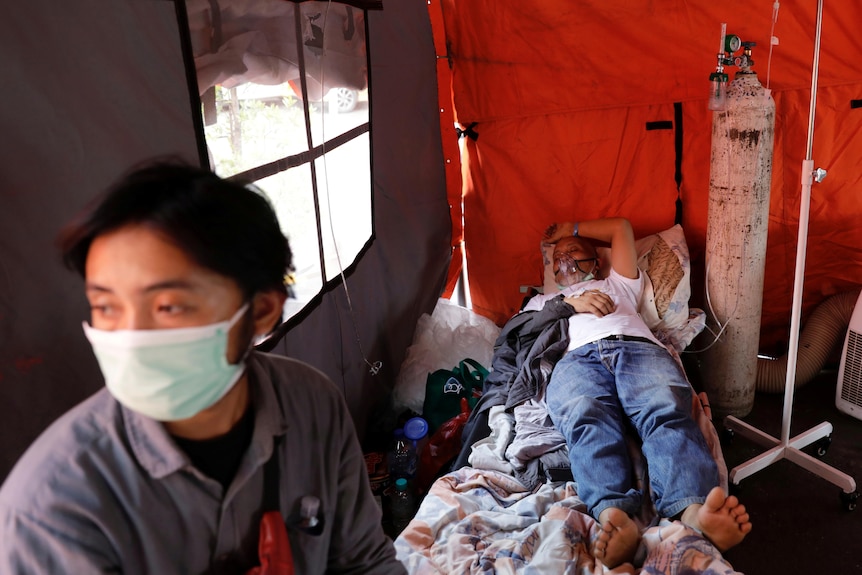 A coronavirus patient rests alongside his son in a temporary tent outside a hospital