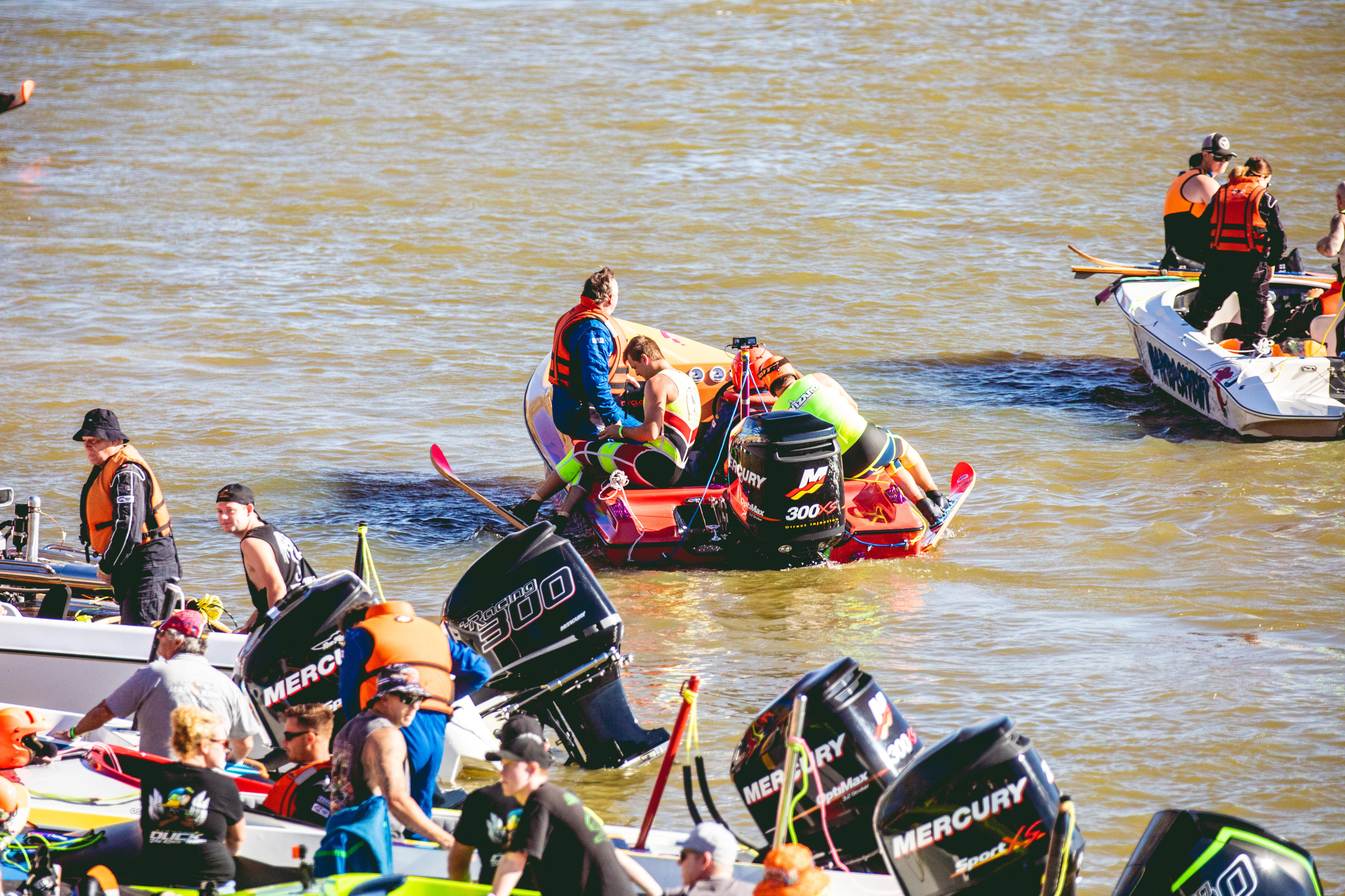 Un barco con un esquiador acuático sentado al lado cerca de varios motores de barcos amarrados en la orilla del río