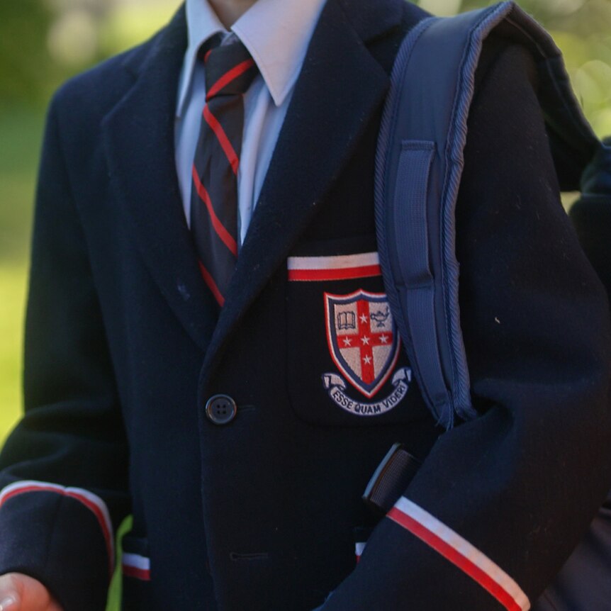 A boy, whose face is not shown, wearing a Cranbrook School blazer and tie, with a backpack over his shoulder.