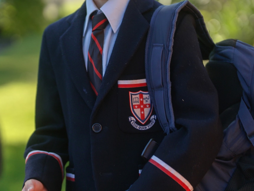 A boy, whose face is not shown, wearing a Cranbrook School blazer and tie, with a backpack over his shoulder.