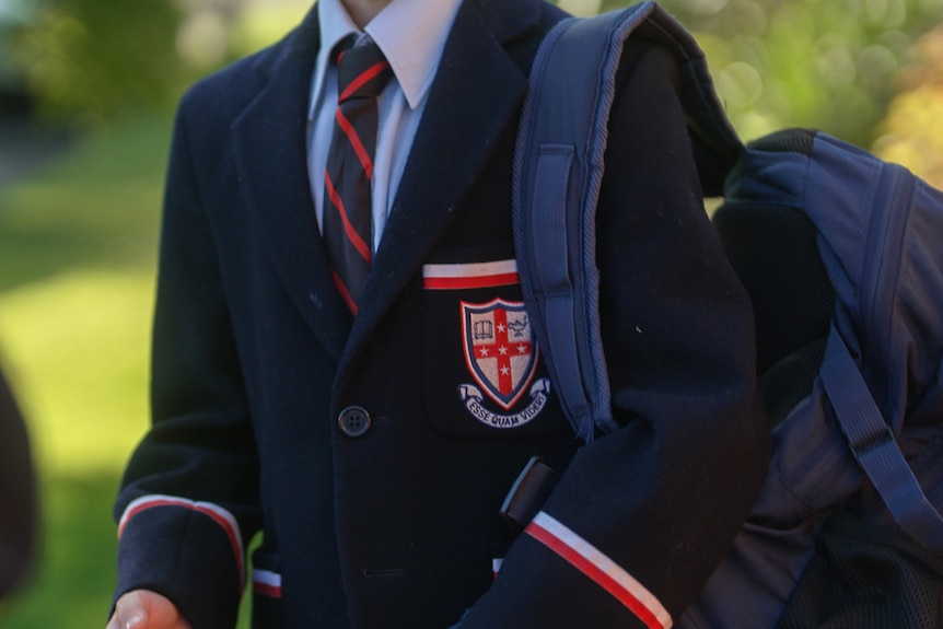 A boy, whose face is not shown, wearing a Cranbrook School blazer and tie, with a backpack over his shoulder.