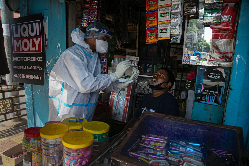 在印度高哈蒂市的一个市场上，一名卫生工作者在对一名店主进行新冠随机检测时，从他的鼻腔里进行拭子取样。