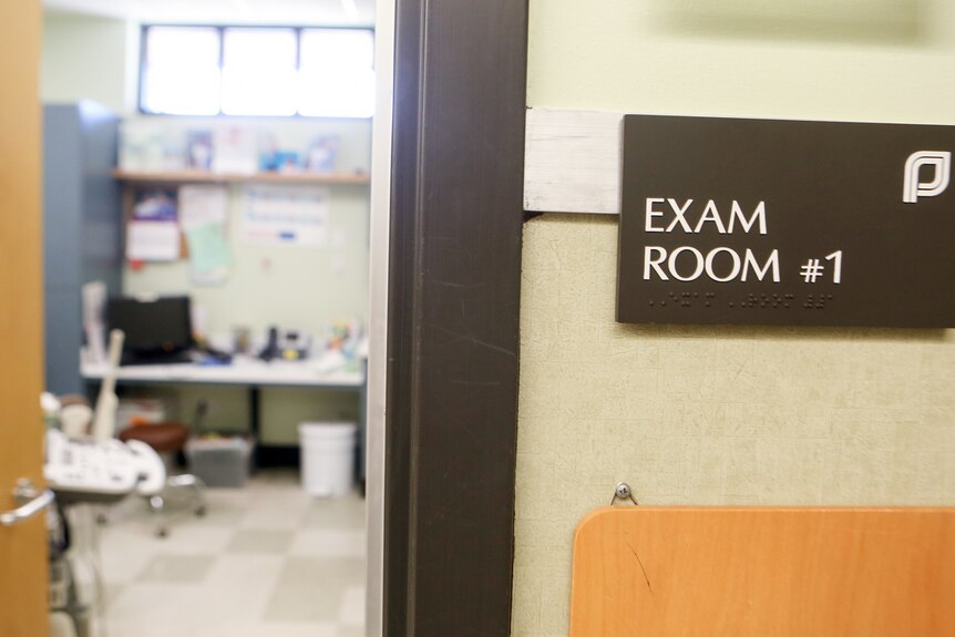 A sign saying Exam Room hangs beside a door to an empty room.