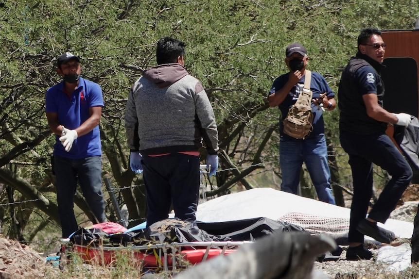 Rescue workers wearing gloves pick up debris at a crash site on a country road