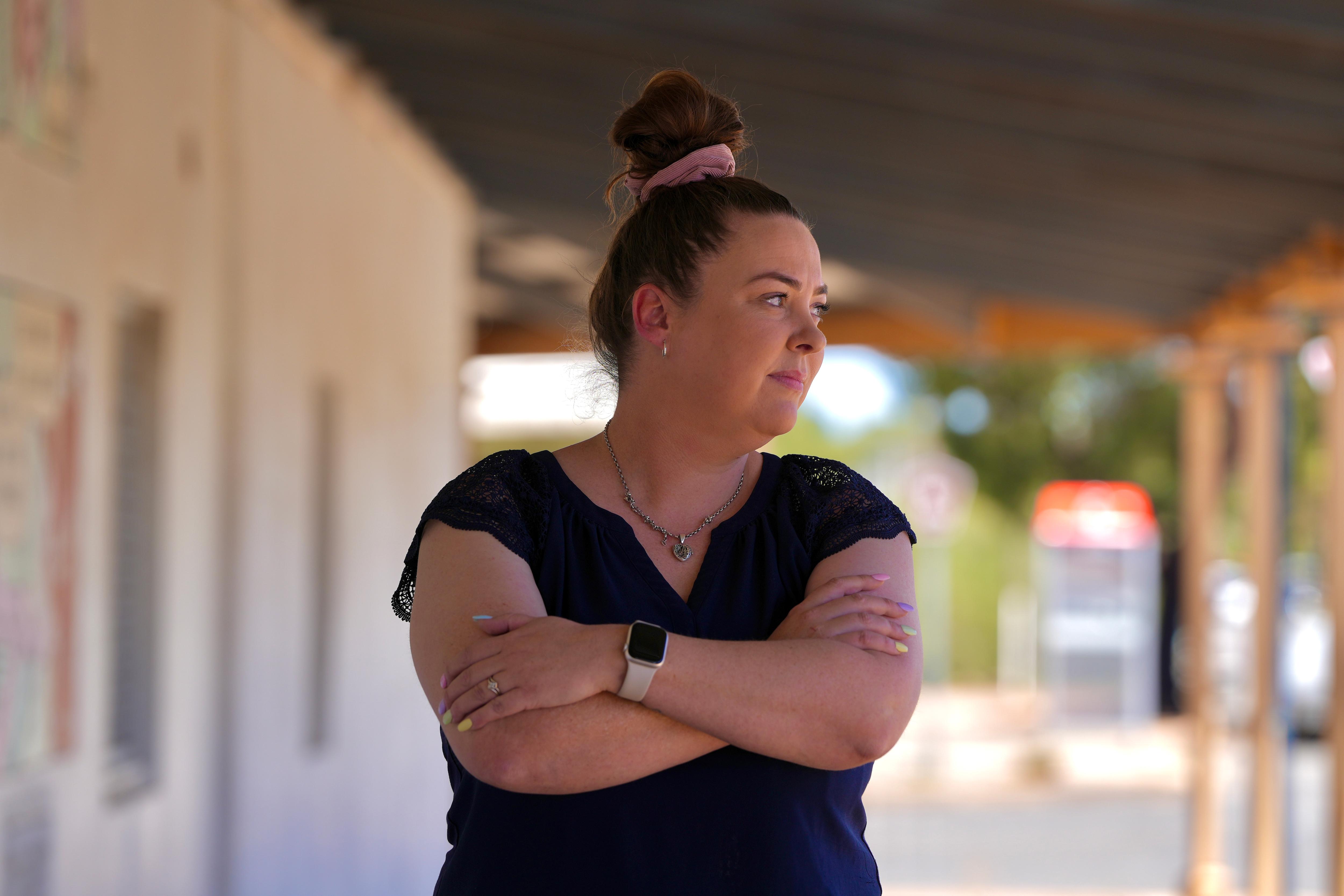 A white woman with brown hair in a bun crossing her arms and looking sideways. 