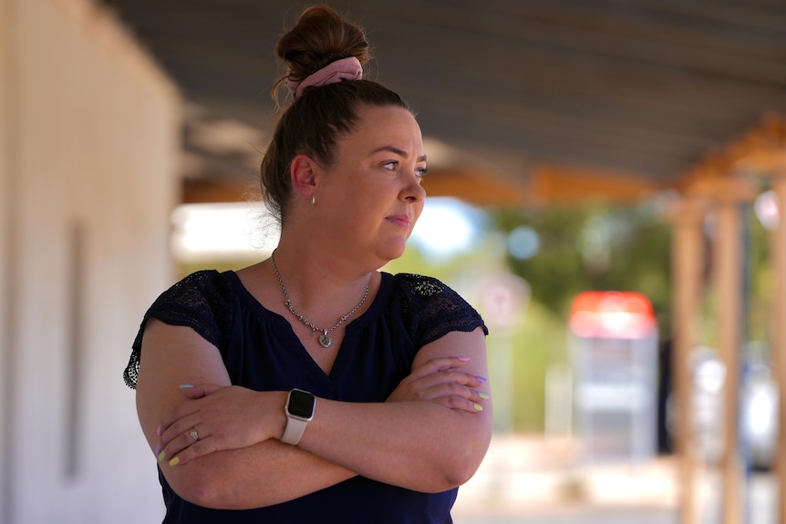 A white woman with brown hair in a bun crossing her arms and looking sideways. 