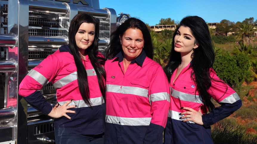 A mother and her two daughters pose in pink high-vis jackets in front of a pink truck.