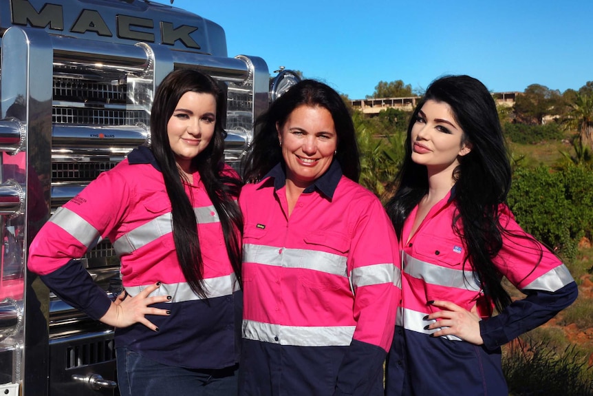 A mother and her two daughters pose in pink high-vis jackets in front of a pink truck.