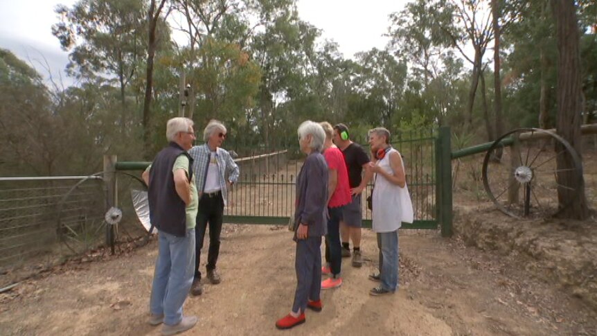 Six people stand at the gate of a home where a security alarm has been ringing non-stop.