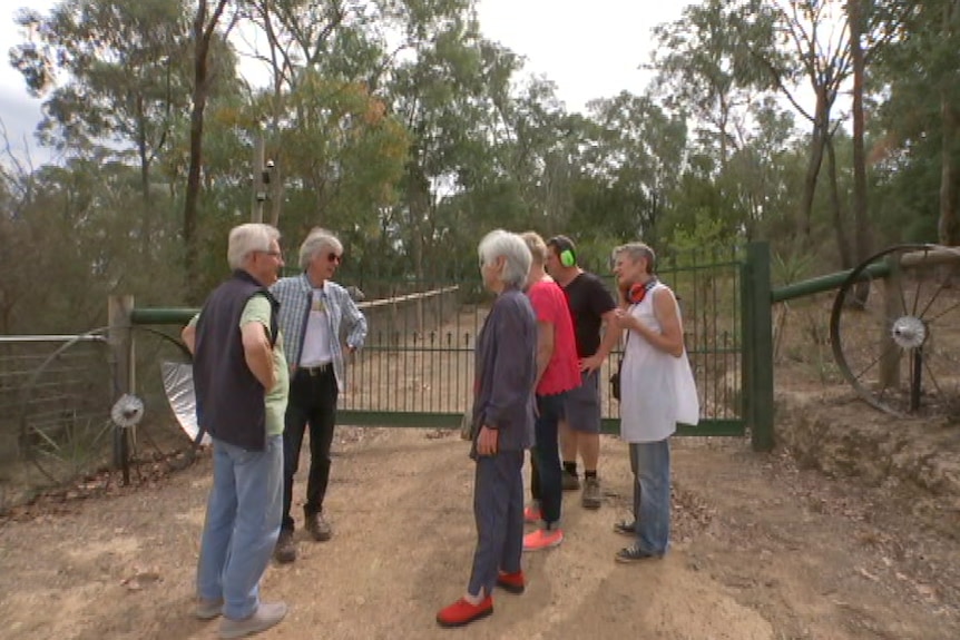 Six people stand at the gate of a home where a security alarm has been ringing non-stop.