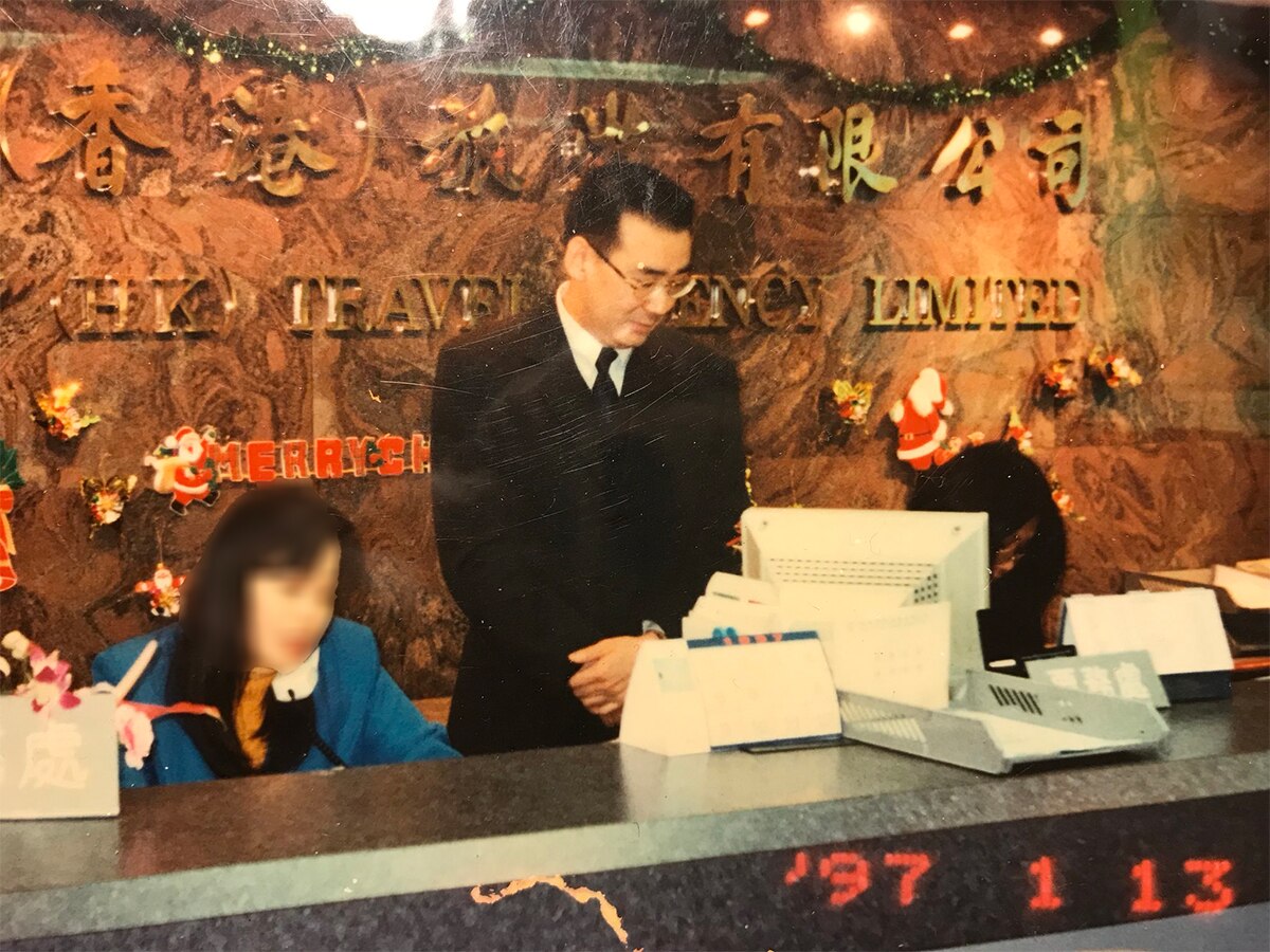 Yang stands behind a tourism desk.