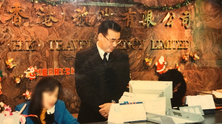 Yang stands behind a tourism desk.