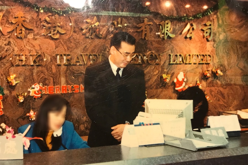 Yang stands behind a tourism desk.