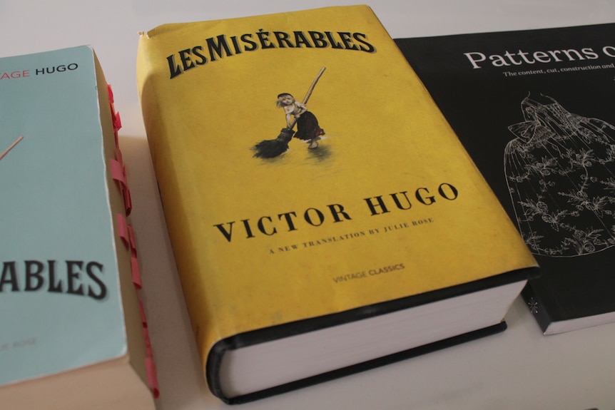 Un épais livre jaune avec les mots Les Misérables et Victor Hugo en noir et l'image d'une jeune fille avec un balai.