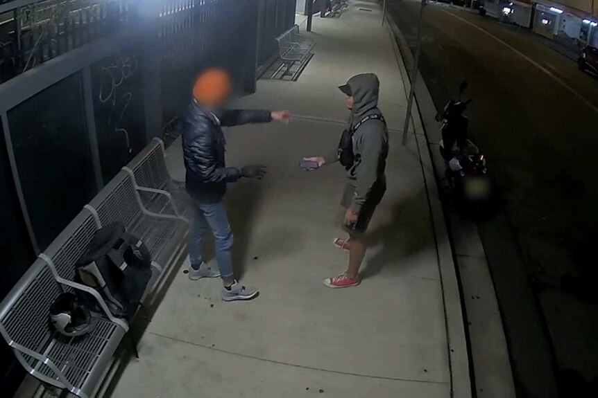 A man in a hoodie confronts a man with a food delivery bag on a bench