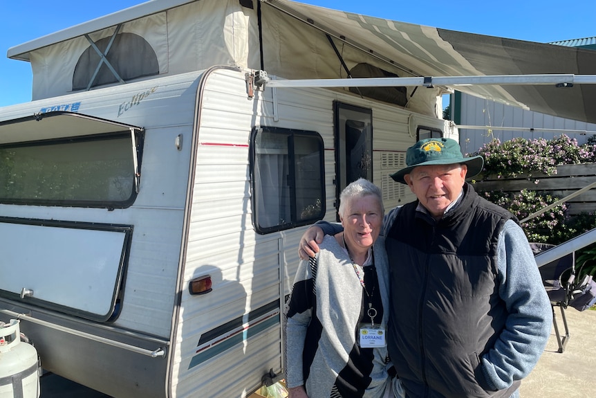 A couple stands next to their caravan.