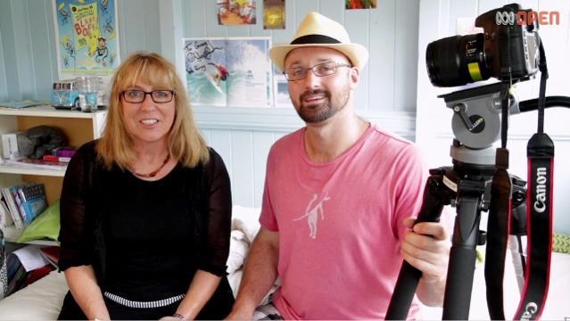 Woman and man sit beside camera on tripod