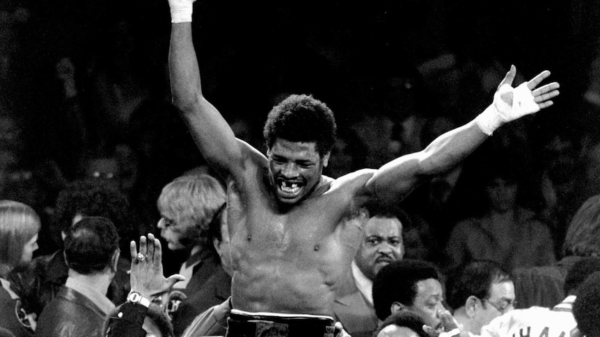 Leon Spinks sits on the shoulders of a group of people with his arms raised above him