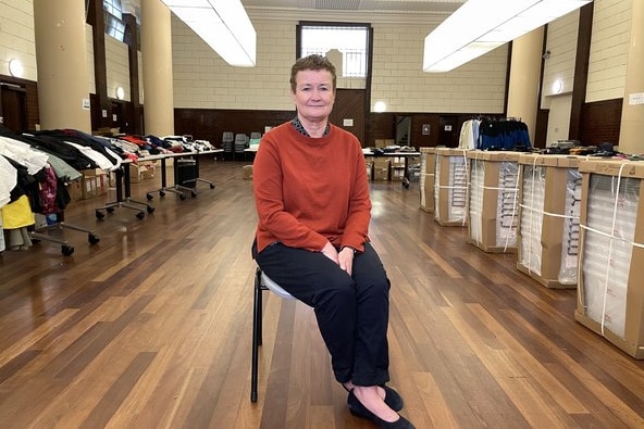 A photo of Catherine sitting on a chair, surrounded by tables full of donated items.