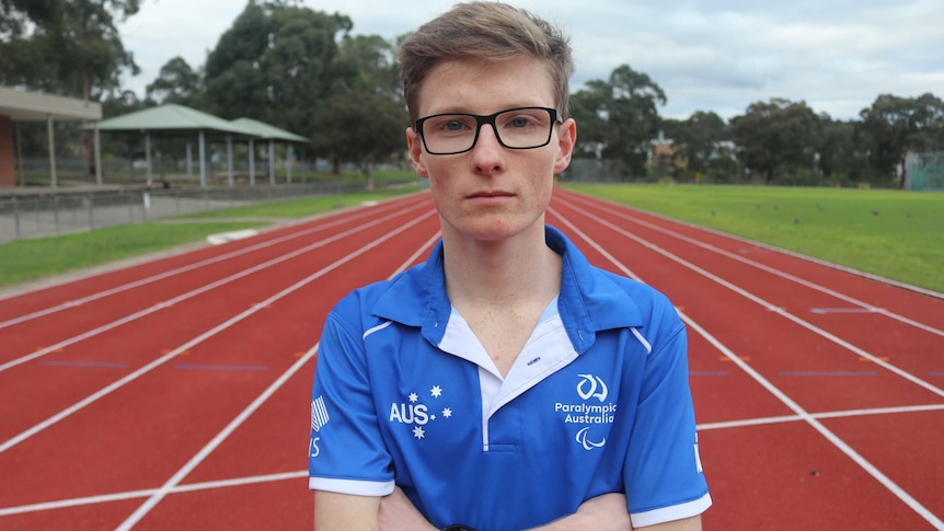 Jaryd Clifford stands in in the middle of a running track wearing a Paralympics Australia shirt.