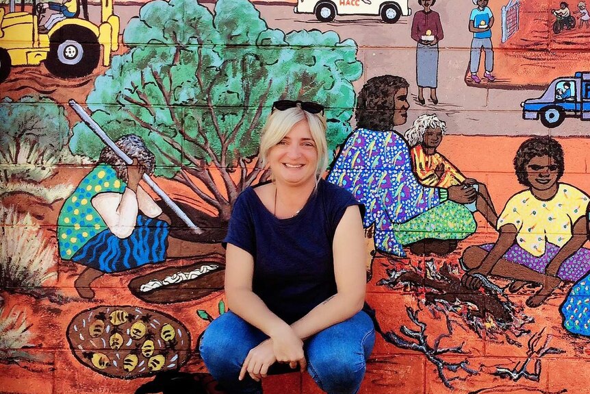 Woman, Mena, crouched in front of colourful mural