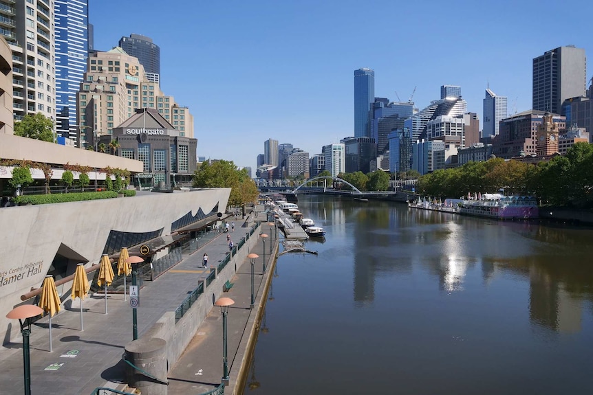 A murky Yarra River lined with empty walkways and a backdrop of skyscrapers