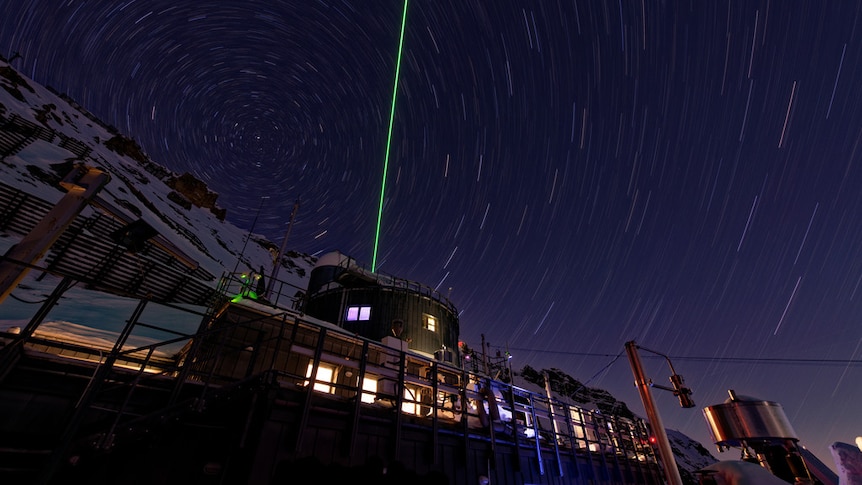 A green laser is fired into a swirling night sky from Schneefernerhaus